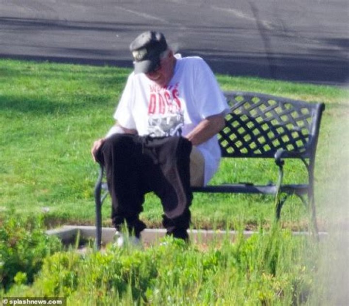 With His Pants At His Knees, Gary Busey Is Pictured Sitting On A Park Seat